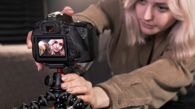 Gros plan d'une jeune femme aux cheveux blonds ajustant une caméra reflex professionnelle montée sur un trépied flexible.