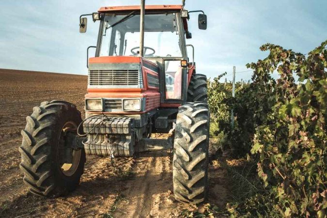 Un gros plan sur un tracteur enjambeur rouge stationné au bord d'une rangée de vignes.