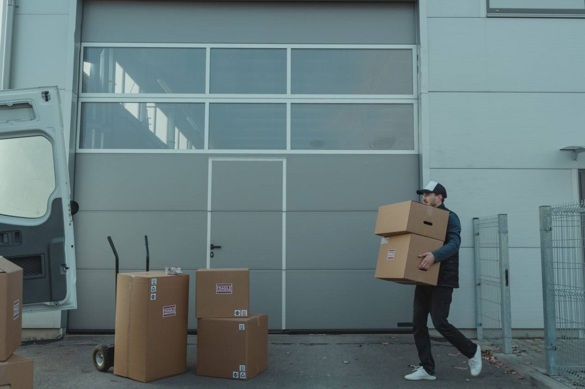 Un homme transporte des cartons de déménagement dans ses bras vers un camion ouvert, illustrant des astuces pour réduire le coût de son déménagement au maximum.