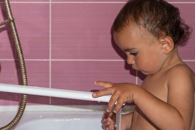 Un enfant joue avec l'eau de la baignoire.