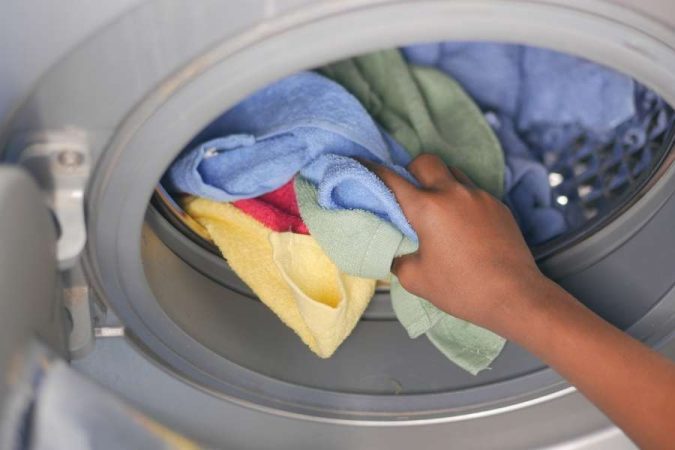 Une main charge du linge coloré dans le tambour d'un lave-linge.