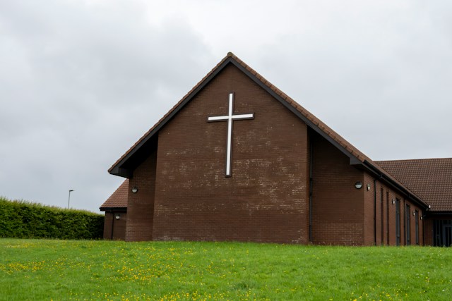 Façade en briques d'une église moderne ornée d'une grande croix blanche sous un ciel couvert.