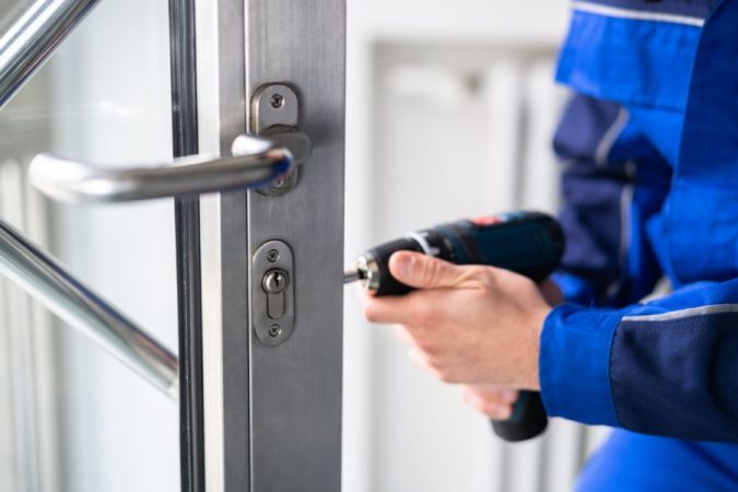 Un artisan réparant une serrure de porte métallique avec une perceuse, une situation pouvant mener à une facturation abusive d'un serrurier.